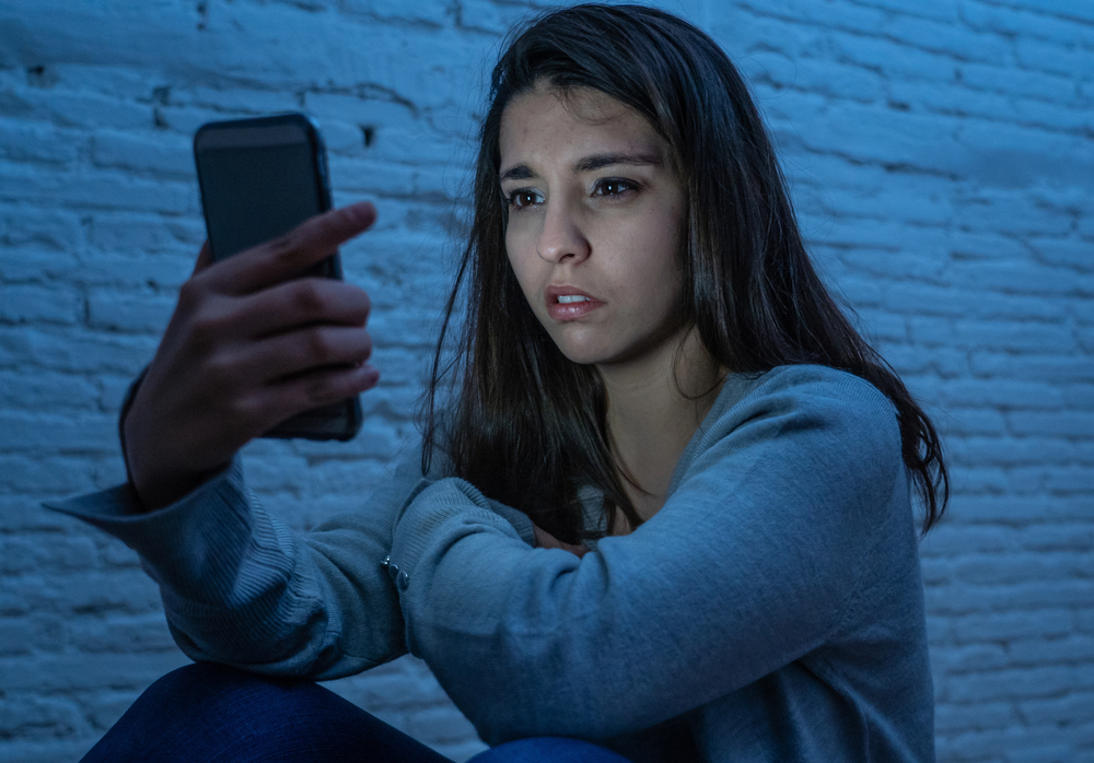 Eine Person hält nachts ein Smartphone in der Hand und wirkt durch wiederholte Anrufe beunruhigt.